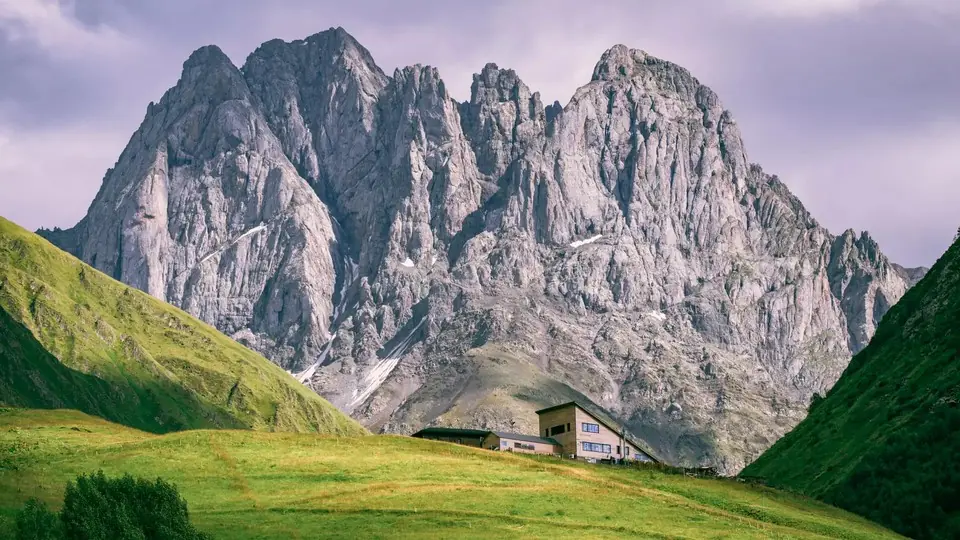 Grey Chaukhi rock towers above a green meadow with a mountain hut