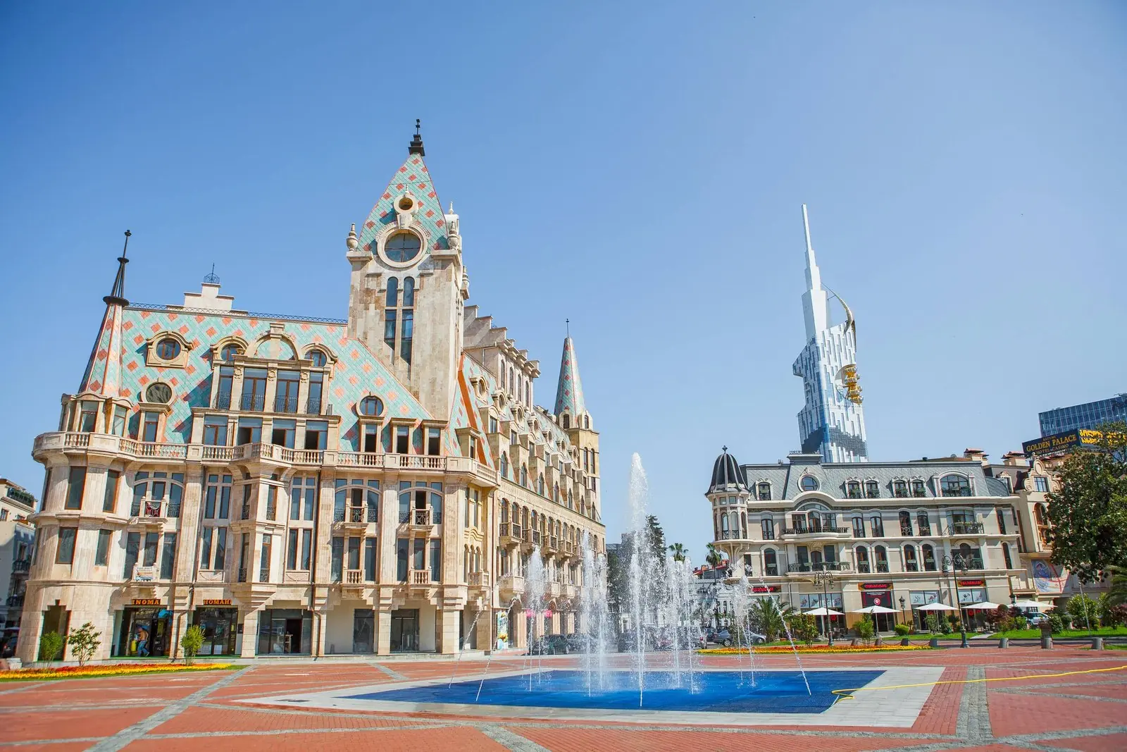 Europe Square in Batumi on a sunny day, with the fountain, a tiled historic-style building with a clock tower and a modern tower on the skyline