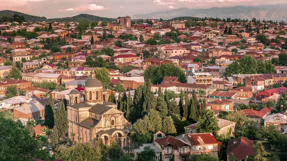 Панорама крыш Кутаиси с купольной церковью среди кипарисов на закате