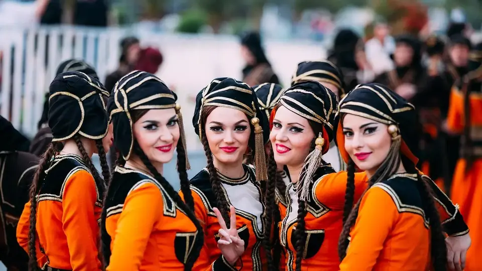 Улыбающиеся девушки в оранжево-черных костюмах для грузинских народных танцев на празднике под открытым небом