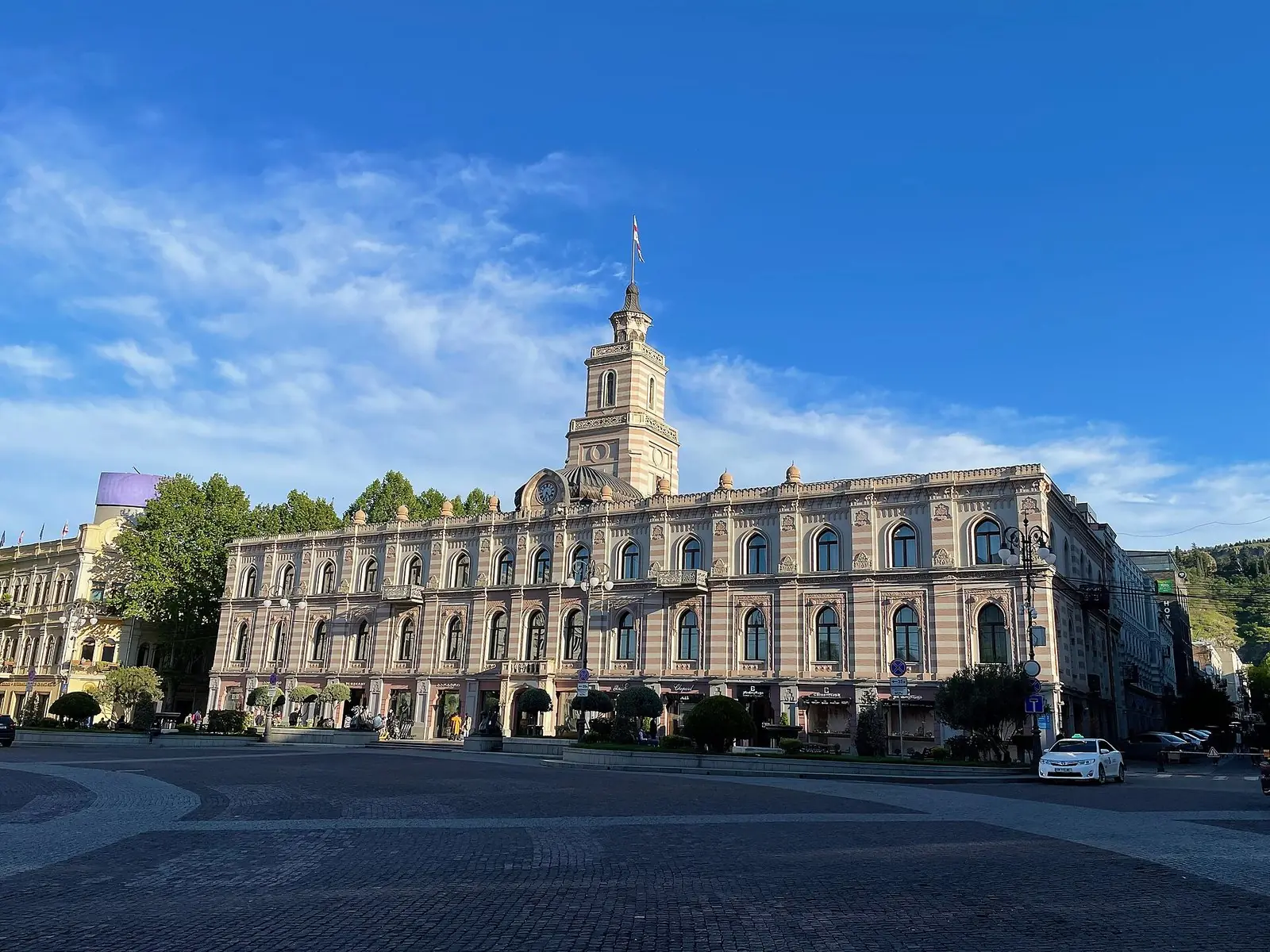 The striped pseudo-Moorish City Hall and its clock tower on Freedom Square in Tbilisi, under a blue sky