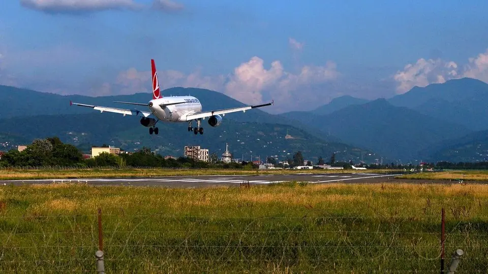A passenger jet about to touch down on the runway at Batumi airport, with green Adjara hills behind