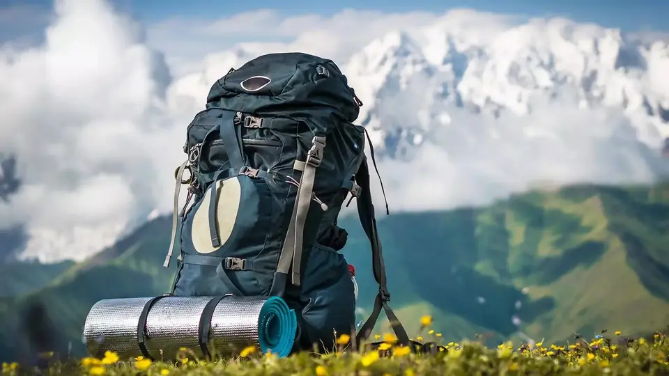 Trekking backpack with sleeping mat in a meadow in front of snowy peaks