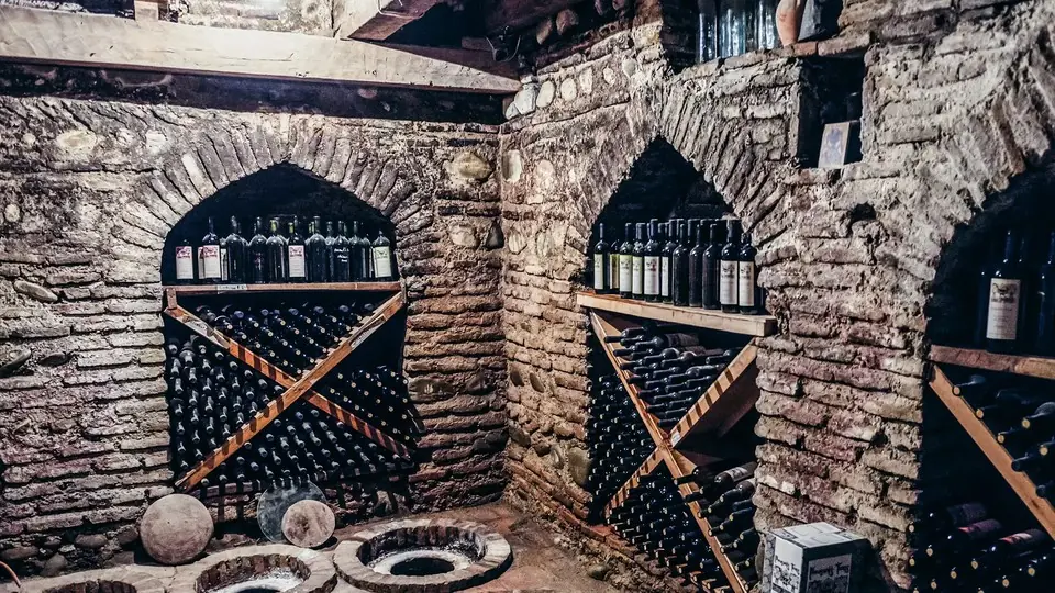 Brick-arched wine cellar with racks of bottles and qvevri lids set in the floor