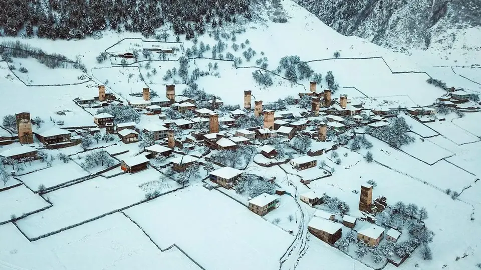 Aerial view of a snow-covered Svan village with stone defence towers and white fields in winter