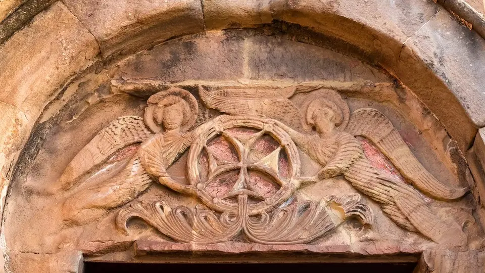 Carved stone tympanum with two angels holding a cross above a church doorway at Jvari