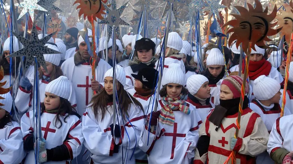 Children in white Alilo robes with red crosses carry stars and sun icons in the Christmas procession in Tbilisi