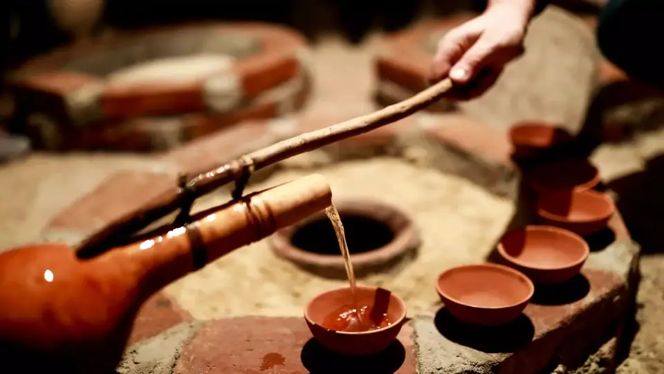 Wine ladled from a buried qvevri with a long gourd ladle into clay cups