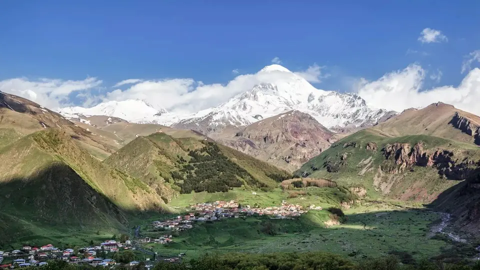 Stepantsminda town in a green valley below snow-capped Mount Kazbek and Gergeti