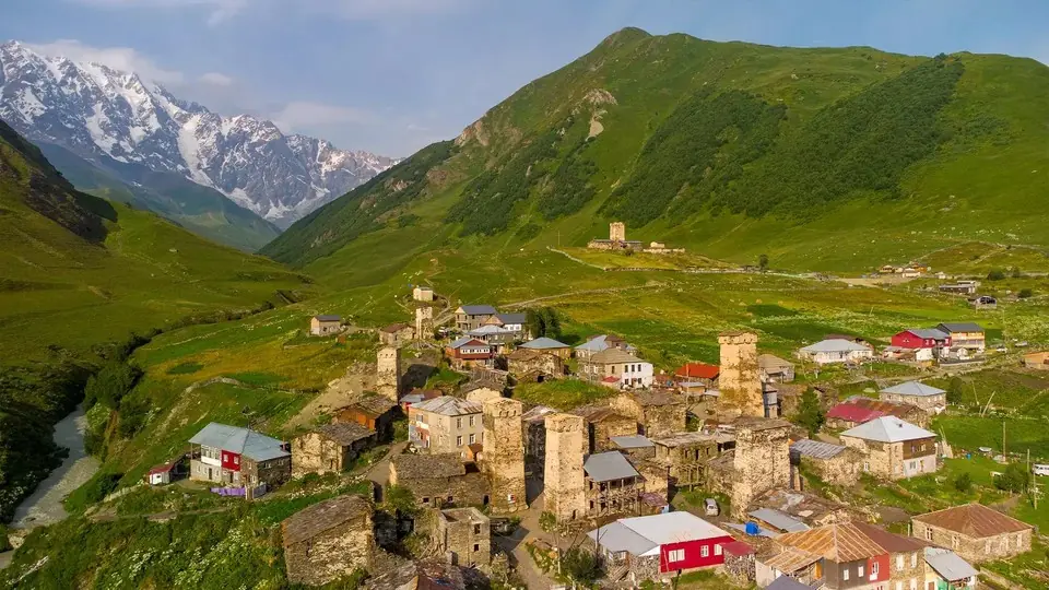 Ushguli village with stone Svan towers in a green valley below the snowy Shkhara massif