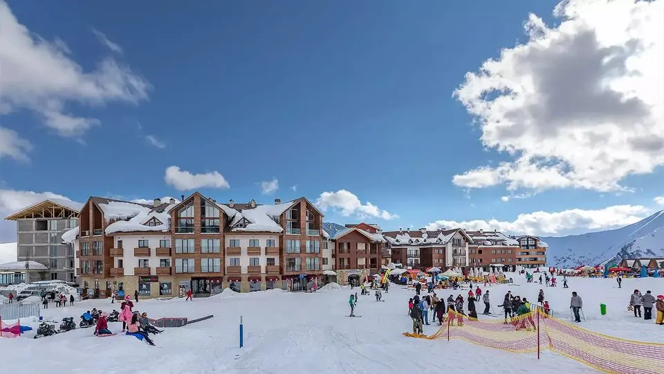 Skiers and holiday crowds on the snowy base area of Gudauri below chalet-style hotels