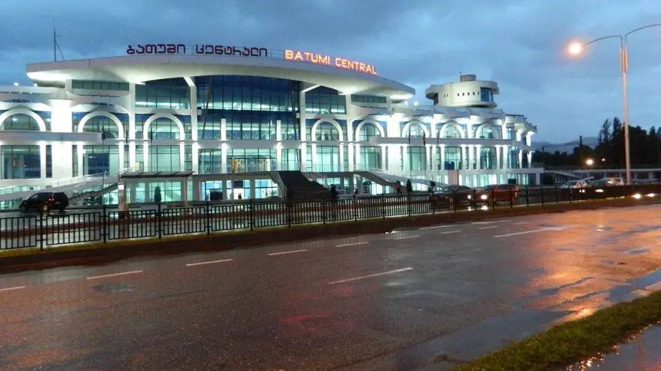 Batumi Central railway station lit up at dusk, its white arched front signed in Georgian and English above a wet road