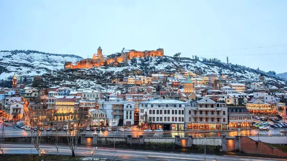 Old Tbilisi and Narikala fortress with light snow on the hills on a winter evening