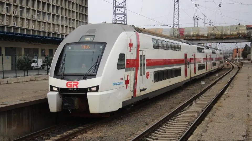 A white and red Stadler double-deck train of Georgian Railway arriving at a Tbilisi platform under overhead wires