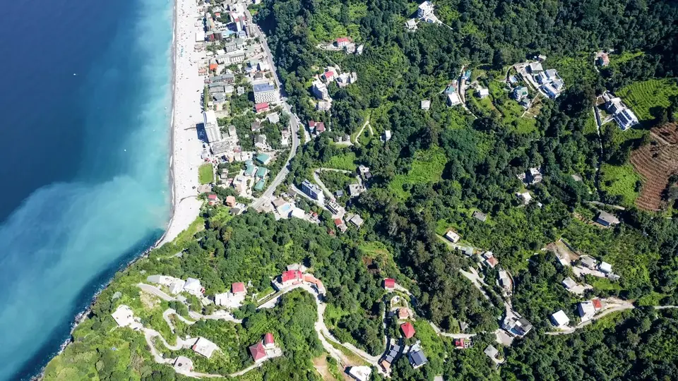 Aerial view of the Black Sea meeting a pebble beach and green hills dotted with houses