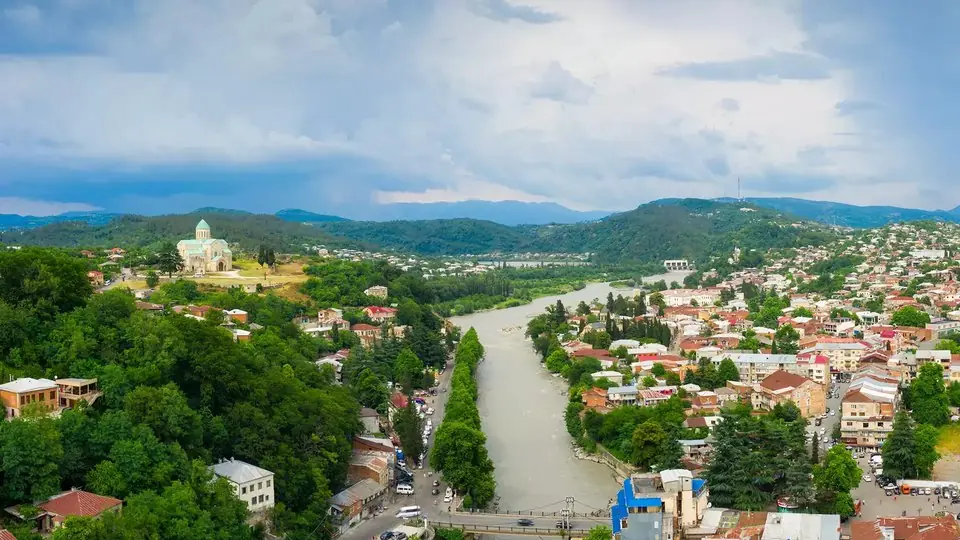 Kutaisi from above: the Rioni river between red-roofed houses on both banks, with Bagrati Cathedral on its green hill to the left
