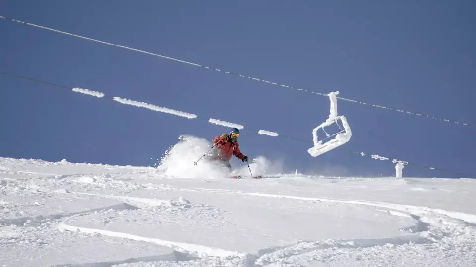 Skier spraying powder snow below a chairlift on a bright winter day
