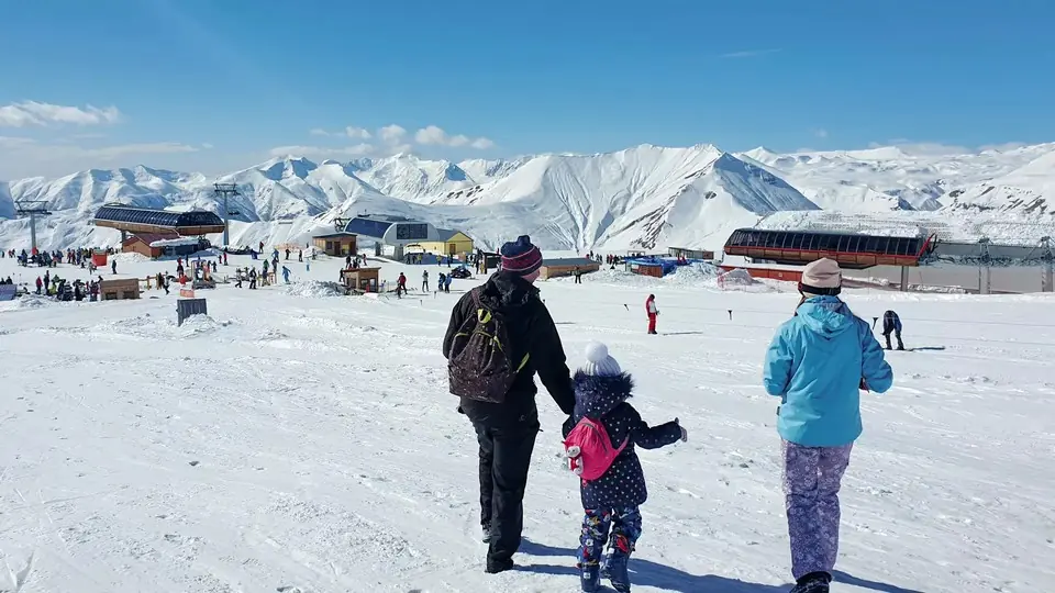 Родители и маленький ребенок гуляют вместе по снегу в Гудаури