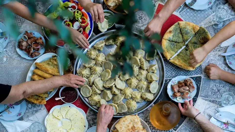Руки тянутся к хинкали, хачапури и мясу на гриле на общем грузинском столе