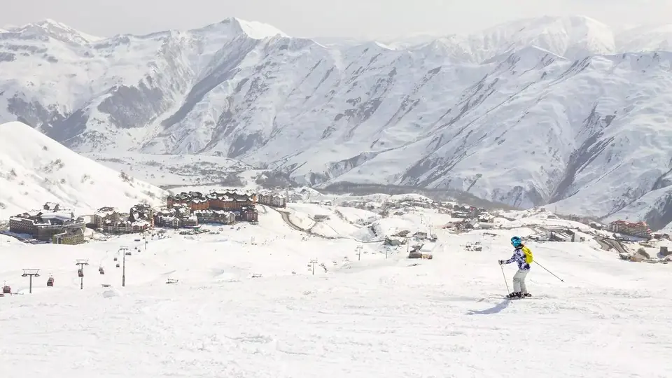 Лыжник на снежном склоне, позади курортный поселок Гудаури