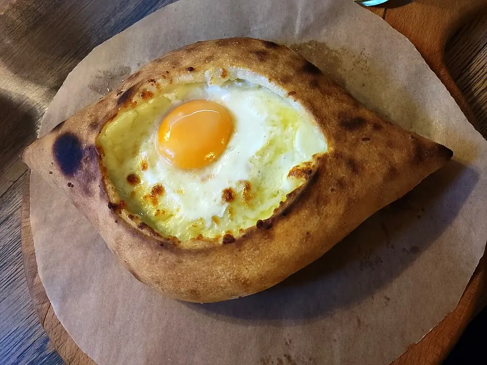 Adjarian khachapuri: a boat-shaped bread filled with melted cheese and a whole egg yolk, served on baking paper on a wooden board