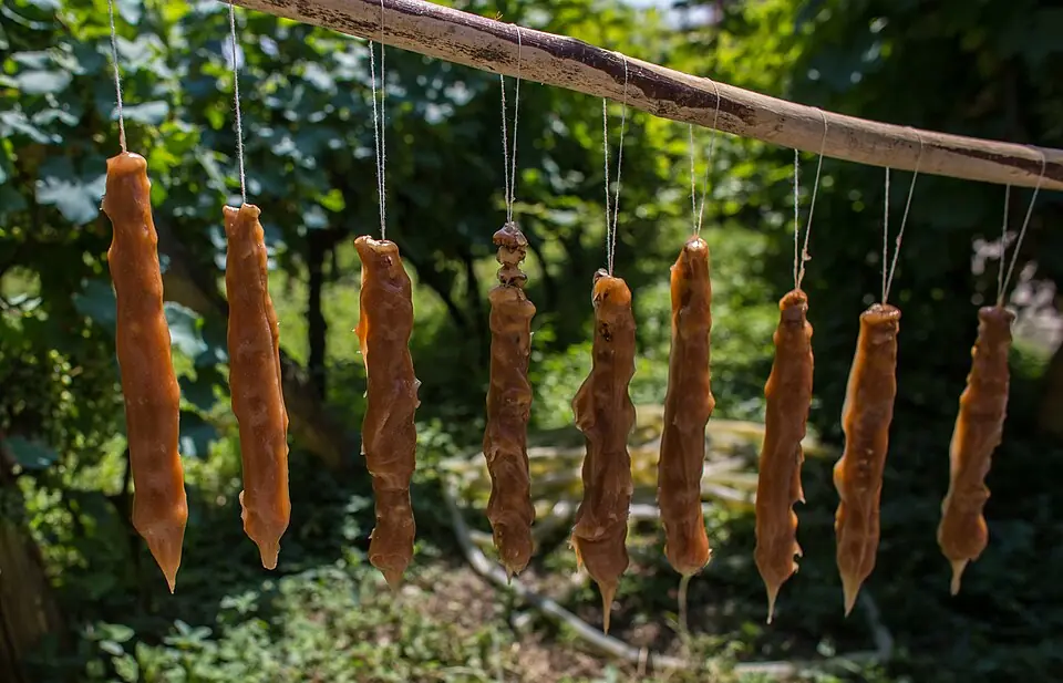 Homemade churchkhela, strings of walnuts coated in thickened grape juice, hanging from a wooden pole to dry in the sun