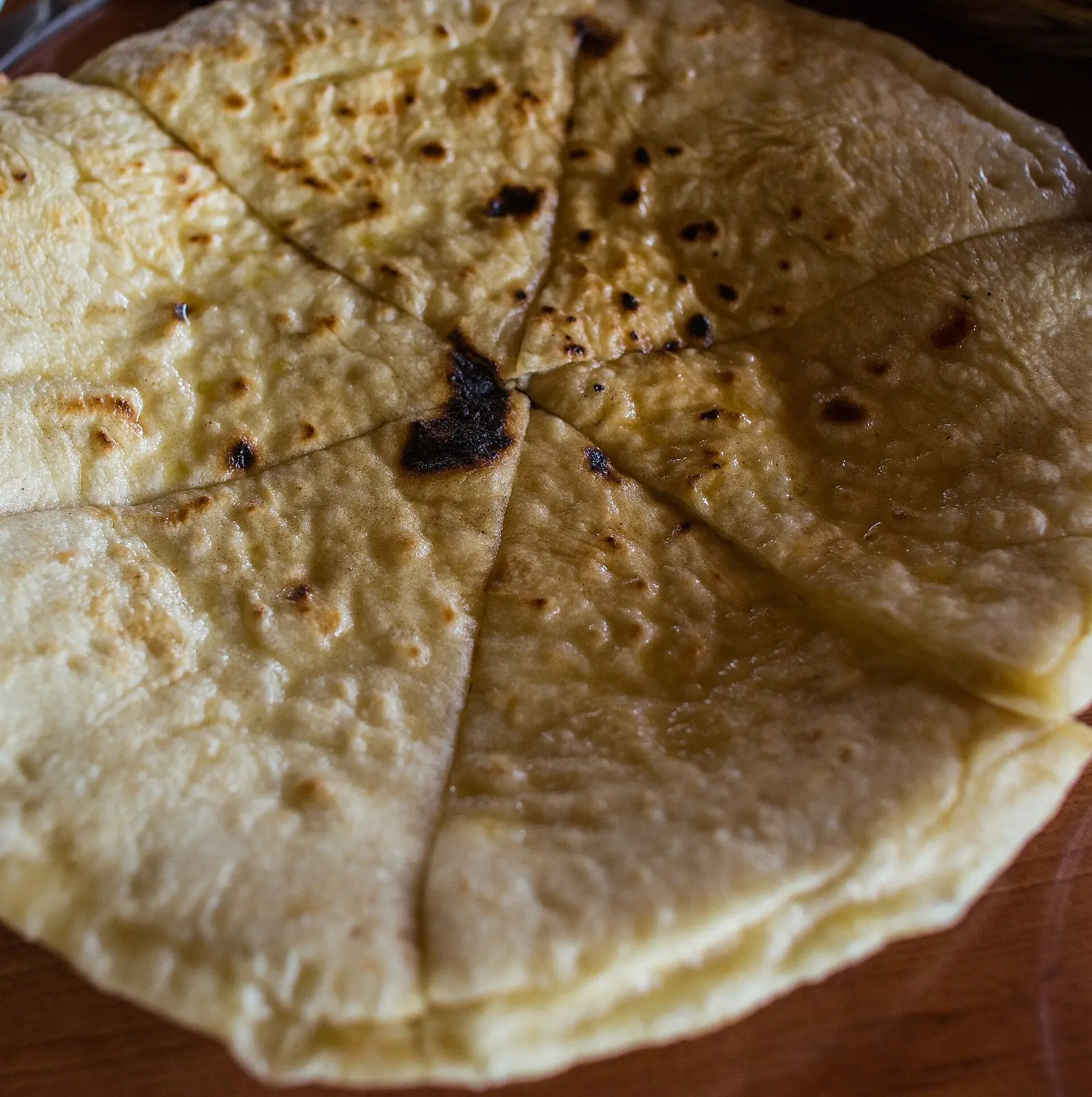 Round Imeruli khachapuri cut into wedges, its pale crust freckled brown from the pan and a thin layer of cheese showing at the cut edges