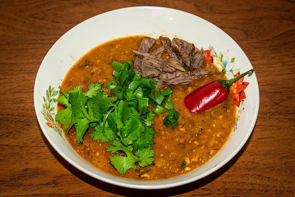 A bowl of thick kharcho soup topped with pieces of slow-cooked beef, chopped coriander, spring onion and a red chilli