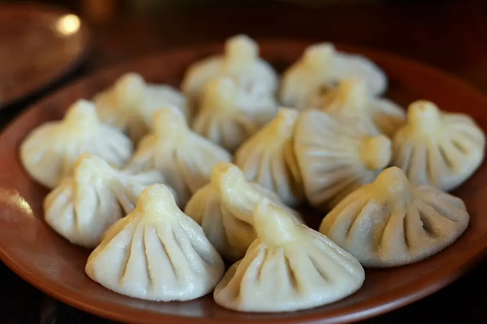 A clay plate of boiled khinkali dumplings with their pleated, knotted tops