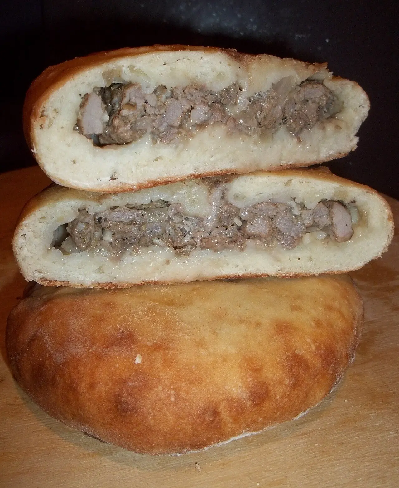 A kubdari cut in half, the two halves stacked on a whole golden round to show the hand-chopped meat filling inside the bread
