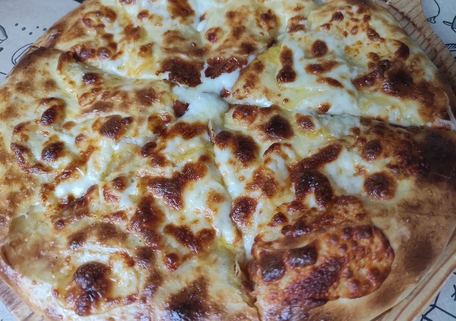 Close-up of a round Megruli khachapuri cut into wedges, its sulguni topping melted and browned in dark blisters over a golden rim, on a wooden board