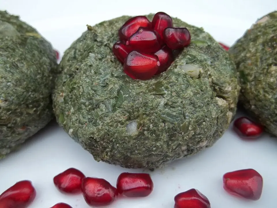 Spinach and walnut pkhali balls topped with pomegranate seeds on a white plate