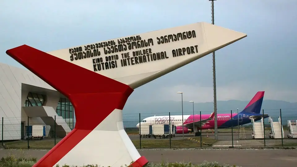 Вывеска Международного аэропорта Кутаиси имени царя Давида Строителя, за ней — авиалайнер на стоянке