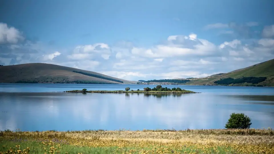 Calm blue Tabatskuri Lake with a small green island and rolling hills