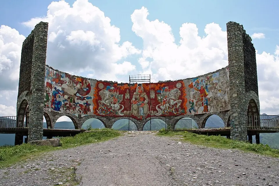 Curved tiled mosaic and stone pylons of the Friendship Monument near Gudauri under summer clouds