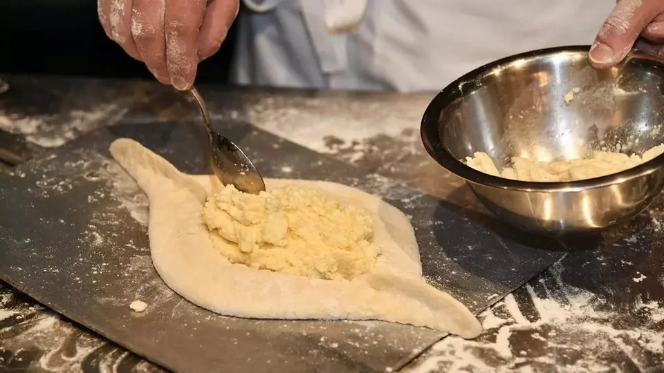 Cook spooning cheese filling into boat-shaped dough for Adjarian khachapuri