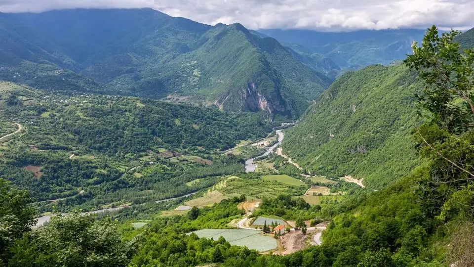 Green mountain valley in Racha with a village and winding road below forested ridges