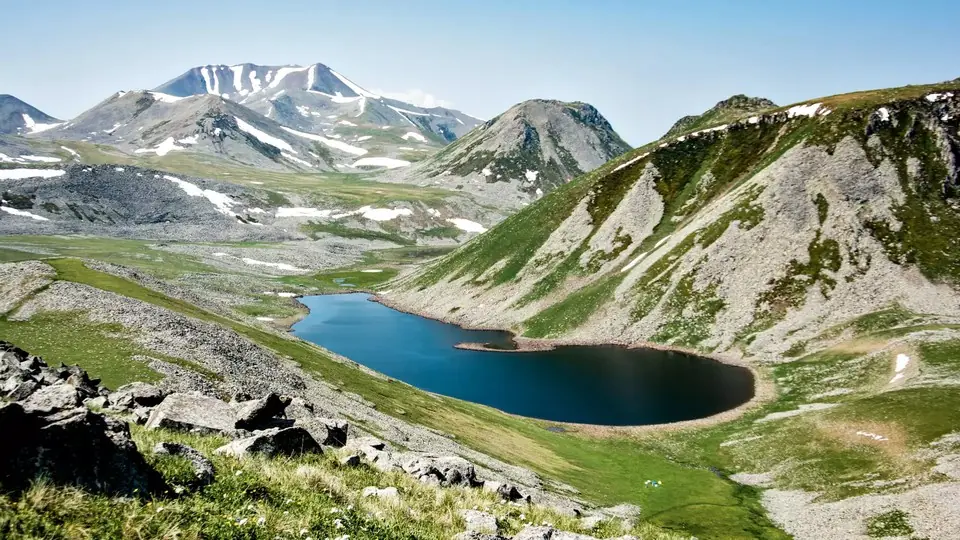Dark crater lake below the grassy, snow-patched slopes of the Samsari volcanic ridge