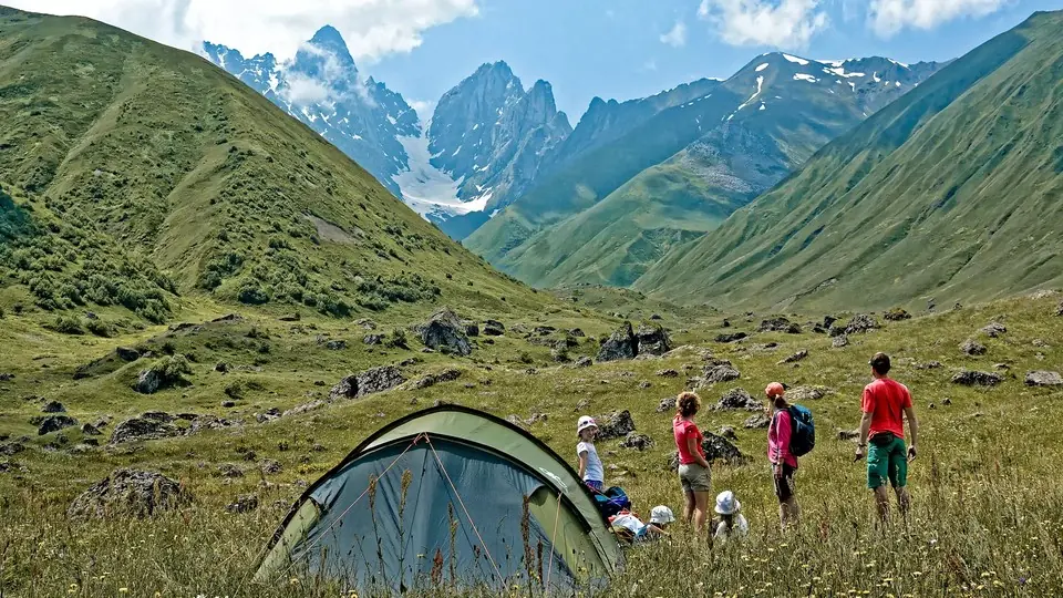 Hikers beside a tent on an alpine meadow below the jagged Chaukhi peaks