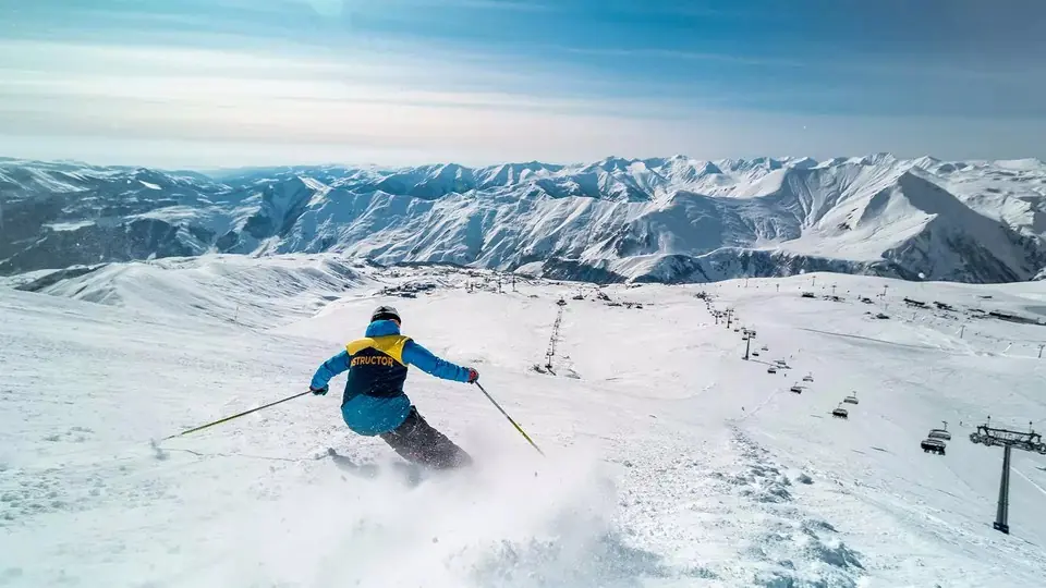 Skier carving through fresh snow at Gudauri with chairlifts and Caucasus peaks behind