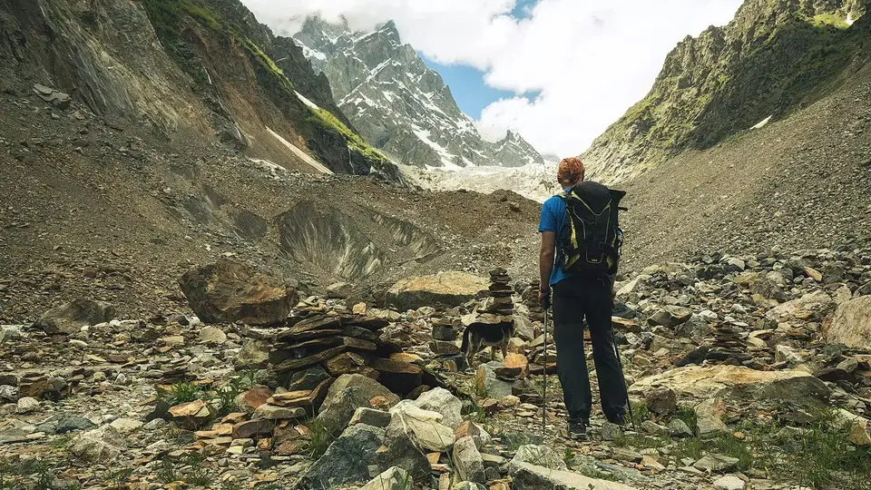 Hiker with a backpack and a dog among stone cairns on the moraine below Chalaadi Glacier