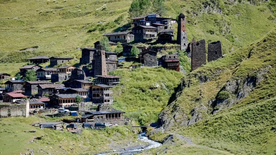 Slate houses and stone towers of Dartlo on a green slope above a stream and footpath