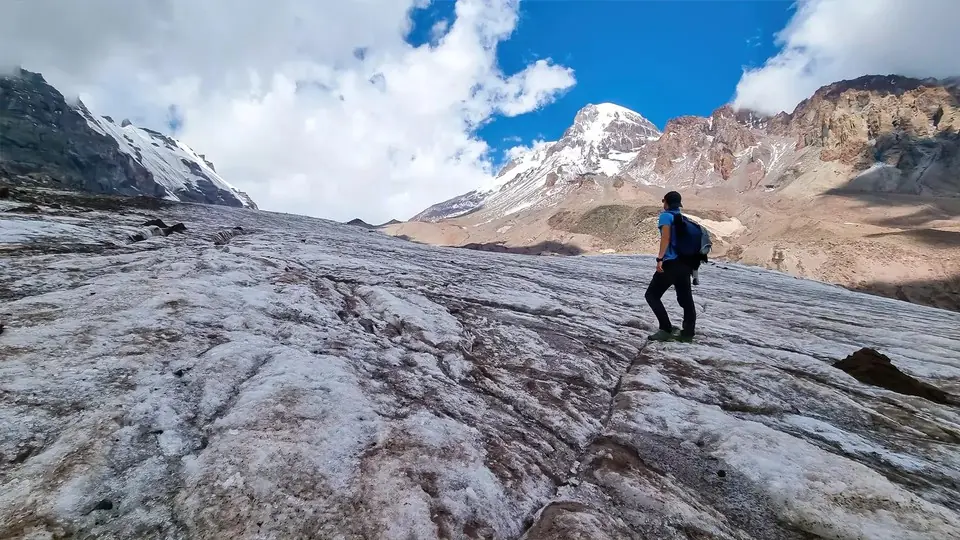 Hiker walking on the ice of the Gergeti Glacier below the snowy cone of Mount Kazbek