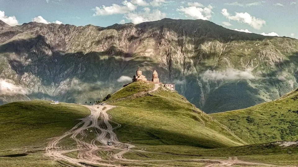 Gergeti Trinity Church on its green saddle with dirt tracks climbing towards it
