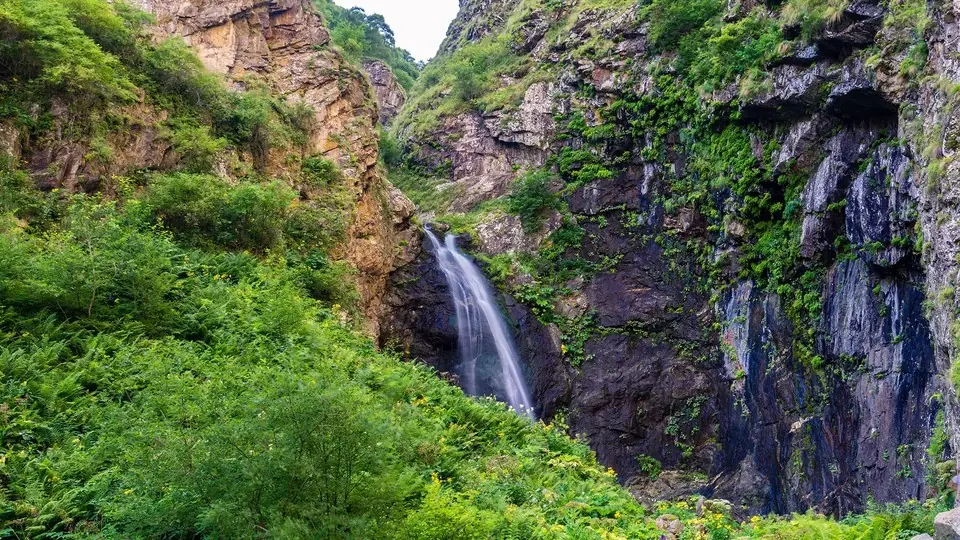 Gveleti waterfall dropping into a green, rocky side gorge of the Dariali valley