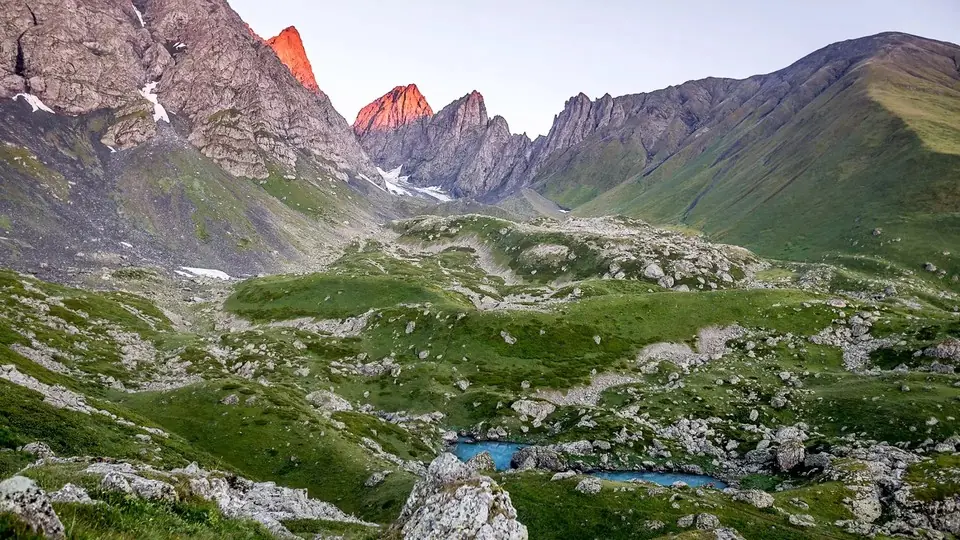 Chaukhi spires glowing red at sunrise above the green, rocky Abudelauri lake basin