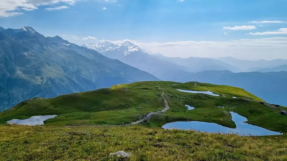 Koruldi tarns on a green plateau with a hiking track, Svaneti peaks fading beyond