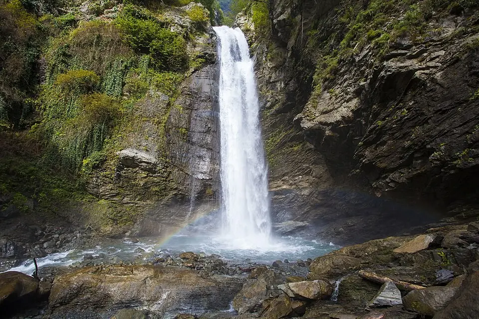 Ninoskhevi waterfall plunging into a pool in a mossy rock amphitheatre, rainbow in spray