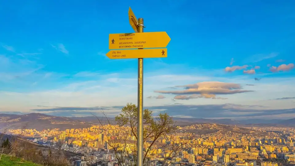 Yellow trail signpost to Turtle Lake and Mtatsminda above Tbilisi at sunset